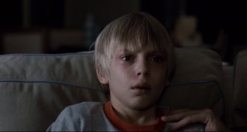 Movie still from “Funny Games” (2007), directed by Michael Haneke – A young boy sitting in a chair with his hand on his chest; Close Up shot, High angle