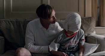 Movie still from “Funny Games” (2007), directed by Michael Haneke – A man and a boy sitting on a couch; Medium shot, Over the shoulder angle