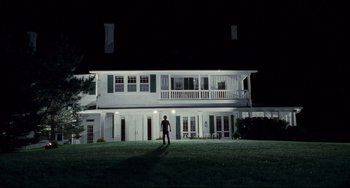 Movie still from “Funny Games” (2007), directed by Michael Haneke – A man standing in the grass in front of a white house at night; Extreme Wide shot, Low angle