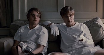 Movie still from “Funny Games” (2007), directed by Michael Haneke – A couple of men sitting next to each other on top of a couch; Medium shot, Low angle