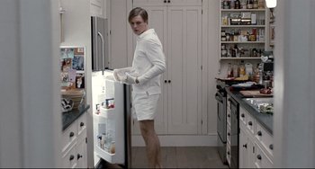 Movie still from “Funny Games” (2007), directed by Michael Haneke – A man standing in front of an open refrigerator in a kitchen; Medium shot, Low angle