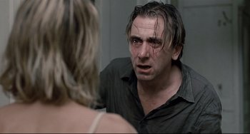 Movie still from “Funny Games” (2007), directed by Michael Haneke – A man looking into a mirror while a woman looks at him; Close Up shot, Over the shoulder angle