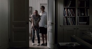 Movie still from “Funny Games” (2007), directed by Michael Haneke – A man and a woman pose for a picture in the doorway; Wide shot, Over the shoulder angle