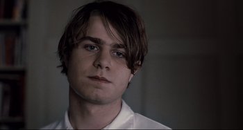 Movie still from “Funny Games” (2007), directed by Michael Haneke – A man with long brown hair wearing a white shirt; Close Up shot, Low angle