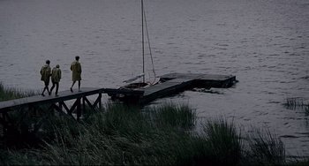 Movie still from “Funny Games” (2007), directed by Michael Haneke – A man standing on a pier next to a boat in a body of water; Extreme Wide shot, High angle