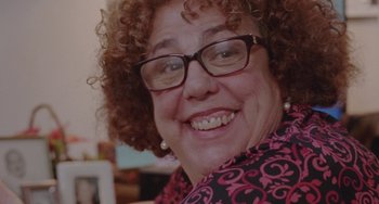Movie still from “Funny Pages” (2022), directed by Owen Kline – A person wearing glasses and smiling; Close Up shot, Over the shoulder angle