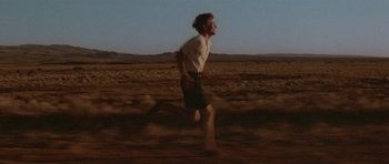Movie still from “Gallipoli” (1981), directed by Peter Weir – A man running across a dry grass field; Wide shot, Low angle