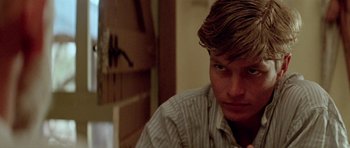 Movie still from “Gallipoli” (1981), directed by Peter Weir – A young man with long blonde hair sitting at a table; Close Up shot, Low angle