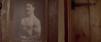 Movie still from “Gallipoli” (1981), directed by Peter Weir – An old picture of a shirtless man hanging on the wall; Extreme Close Up shot, Low angle