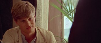 Movie still from “Gallipoli” (1981), directed by Peter Weir – A man sitting in front of a plant in front of a window; Close Up shot, Over the shoulder angle