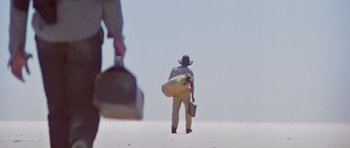 Movie still from “Gallipoli” (1981), directed by Peter Weir – A man in a cowboy hat carrying a bag and a shovel; Wide shot, Low angle