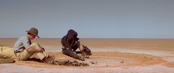 Movie still from “Gallipoli” (1981), directed by Peter Weir – A man sitting on the ground in the desert; Wide shot, High angle