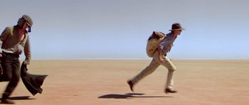 Movie still from “Gallipoli” (1981), directed by Peter Weir – A man running across the desert with a backpack; Wide shot, Low angle