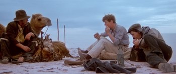 Movie still from “Gallipoli” (1981), directed by Peter Weir – A man sitting on the beach eating something; Wide shot, Low angle