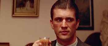 Movie still from “Gallipoli” (1981), directed by Peter Weir – A person holding a drink in a glass; Close Up shot, Over the shoulder angle