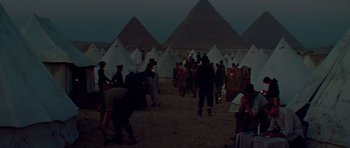 Movie still from “Gallipoli” (1981), directed by Peter Weir – A group of people standing around tents in the desert; Extreme Wide shot, High angle