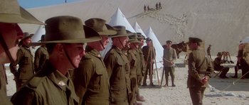 Movie still from “Gallipoli” (1981), directed by Peter Weir – A group of men standing next to each other on a beach; Wide shot, Low angle