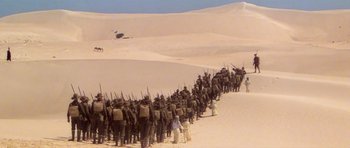 Movie still from “Gallipoli” (1981), directed by Peter Weir – A large group of men are standing in the sand; Extreme Wide shot, High angle