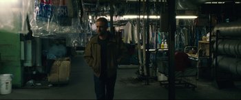 Movie still from “Galveston” (2018), directed by Mélanie Laurent – A man standing in a room with a lot of clothes hanging on the wall; Medium shot, Over the shoulder angle
