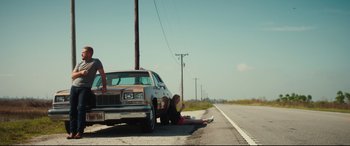 Movie still from “Galveston” (2018), directed by Mélanie Laurent – A woman sitting on the side of a road next to a car; Wide shot, Low angle