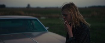 Movie still from “Galveston” (2018), directed by Mélanie Laurent – A woman smoking a cigarette while standing next to a car; Medium shot, Over the shoulder angle