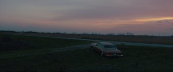 Movie still from “Galveston” (2018), directed by Mélanie Laurent – An old car parked in a grassy field at dusk; Extreme Wide shot, Low angle