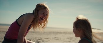 Movie still from “Galveston” (2018), directed by Mélanie Laurent – A woman is laughing on the beach with a surfboard in the background; Medium shot, Over the shoulder angle