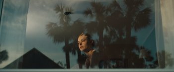 Movie still from “Galveston” (2018), directed by Mélanie Laurent – A woman sitting in front of palm trees looking out a window; Medium shot, Low angle