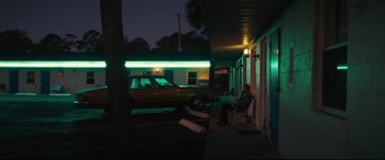 Movie still from “Galveston” (2018), directed by Mélanie Laurent – A man sitting on a chair in front of a motel room; Wide shot, Over the shoulder angle
