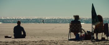 Movie still from “Galveston” (2018), directed by Mélanie Laurent – A person sitting in a lawn chair on the beach; Extreme Wide shot, High angle