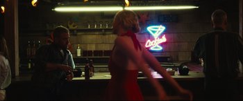 Movie still from “Galveston” (2018), directed by Mélanie Laurent – A woman in a red dress standing in front of a neon sign; Medium shot, Over the shoulder angle