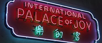 Movie still from “Gambit” (1966), directed by Ronald Neame – A neon sign that reads " international palace of fun "; Wide shot, Low angle