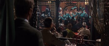 Movie still from “Gambit” (1966), directed by Ronald Neame – A group of people sitting at tables in front of a stage; Wide shot, Over the shoulder angle