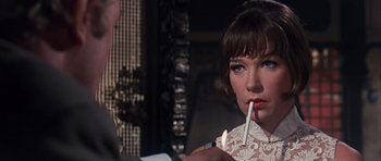 Movie still from “Gambit” (1966), directed by Ronald Neame – A woman lighting a candle while a man looks on; Close Up shot, Over the shoulder angle