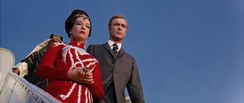 Movie still from “Gambit” (1966), directed by Ronald Neame – A man and a woman standing next to each other in front of a building; Medium shot, Low angle