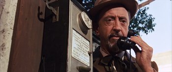 Movie still from “Gambit” (1966), directed by Ronald Neame – A man with a hat and a microphone in front of a wall; Close Up shot, Low angle