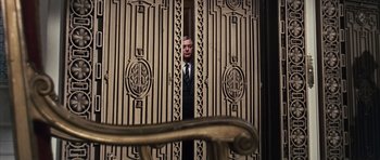 Movie still from “Gambit” (1966), directed by Ronald Neame – A man in a suit and tie standing in front of an open door; Medium shot, Low angle