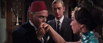 Movie still from “Gambit” (1966), directed by Ronald Neame – A man and a woman in a suit and a woman in a red hat; Medium shot, Over the shoulder angle