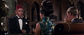 Movie still from “Gambit” (1966), directed by Ronald Neame – A woman in a green dress is sitting in front of a man; Medium shot, Over the shoulder angle