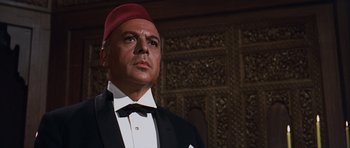 Movie still from “Gambit” (1966), directed by Ronald Neame – A person wearing a suit and tie; Medium shot, Low angle