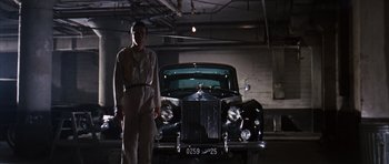 Movie still from “Gambit” (1966), directed by Ronald Neame – A man standing in front of an antique car; Wide shot, Low angle