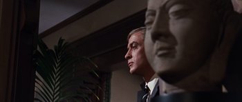 Movie still from “Gambit” (1966), directed by Ronald Neame – A person wearing a suit and tie; Close Up shot, Low angle