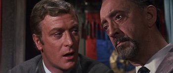 Movie still from “Gambit” (1966), directed by Ronald Neame – A man and a man looking at each other in a room; Close Up shot, Over the shoulder angle