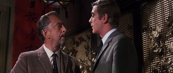 Movie still from “Gambit” (1966), directed by Ronald Neame – A man in a suit talking to another man in a suit; Close Up shot, Low angle