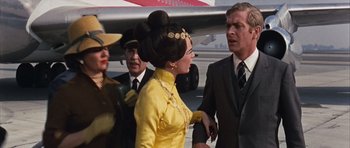 Movie still from “Gambit” (1966), directed by Ronald Neame – A group of people standing next to each other near an airplane; Medium shot, Over the shoulder angle