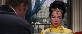 Movie still from “Gambit” (1966), directed by Ronald Neame – A woman in a yellow dress is standing next to a man in a suit; Close Up shot, Over the shoulder angle