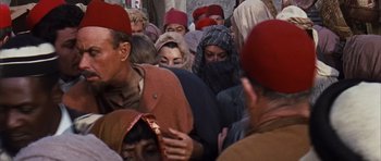 Movie still from “Gambit” (1966), directed by Ronald Neame – A group of people wearing red hats in a crowd of people; Medium shot, High angle