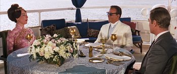 Movie still from “Gambit” (1966), directed by Ronald Neame – A man sitting at a table with a plate of food; Wide shot, Over the shoulder angle