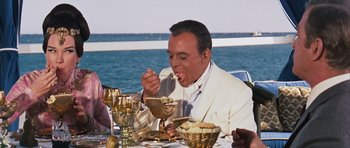 Movie still from “Gambit” (1966), directed by Ronald Neame – A man in a white suit is eating a meal; Medium shot, High angle