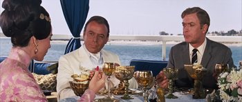 Movie still from “Gambit” (1966), directed by Ronald Neame – A group of people sitting at a dinner table; Medium shot, Over the shoulder angle